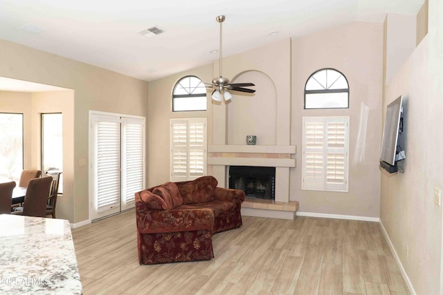 living room featuring ceiling fan, high vaulted ceiling, light wood-style flooring, a fireplace, and baseboards