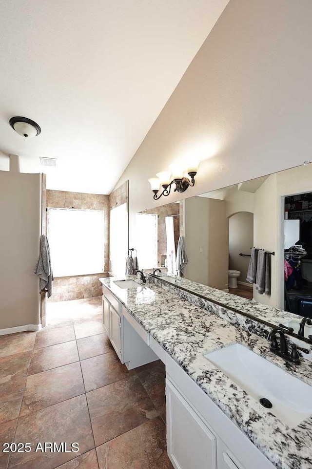 full bath featuring vaulted ceiling, double vanity, a sink, and toilet