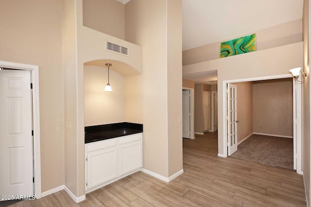 interior space featuring wood finish floors, french doors, visible vents, a towering ceiling, and baseboards