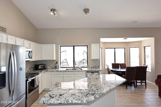 kitchen with stainless steel appliances, a sink, white cabinetry, light wood-style floors, and light stone countertops