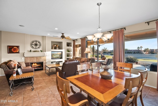 dining room with a water view, built in shelves, a tiled fireplace, and light tile patterned flooring