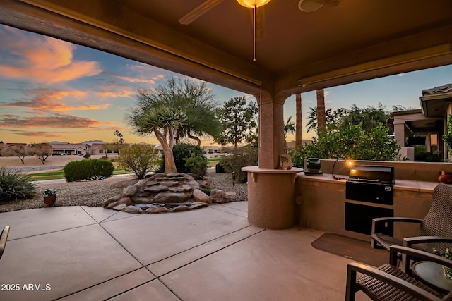 patio terrace at dusk featuring a ceiling fan, exterior kitchen, and area for grilling