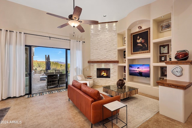 tiled living room with ceiling fan, a stone fireplace, and built in shelves