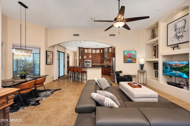 tiled living room with ceiling fan with notable chandelier and built in features