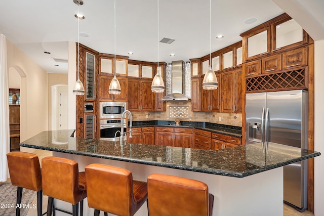 kitchen with wall chimney range hood, stainless steel appliances, a kitchen bar, and pendant lighting