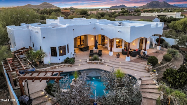 back house at dusk featuring a mountain view, a patio area, and a pool with hot tub