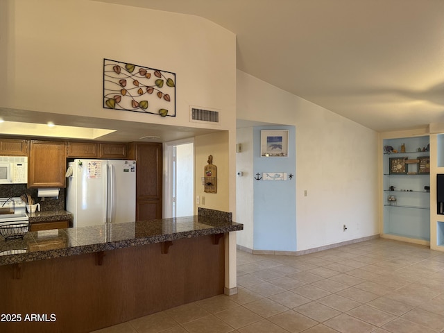 kitchen with white appliances, tile countertops, light tile patterned floors, visible vents, and a kitchen bar