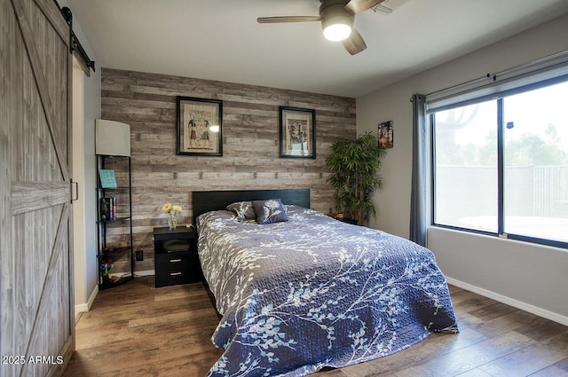 bedroom featuring wooden walls, baseboards, wood finished floors, and an accent wall