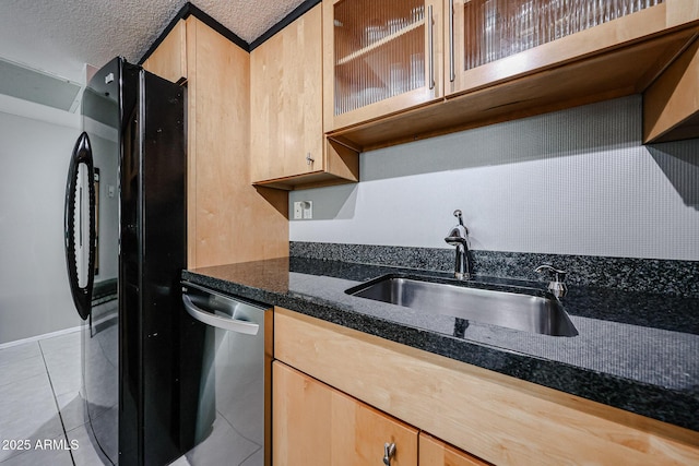 kitchen featuring light brown cabinetry, dishwasher, light tile patterned floors, freestanding refrigerator, and a sink