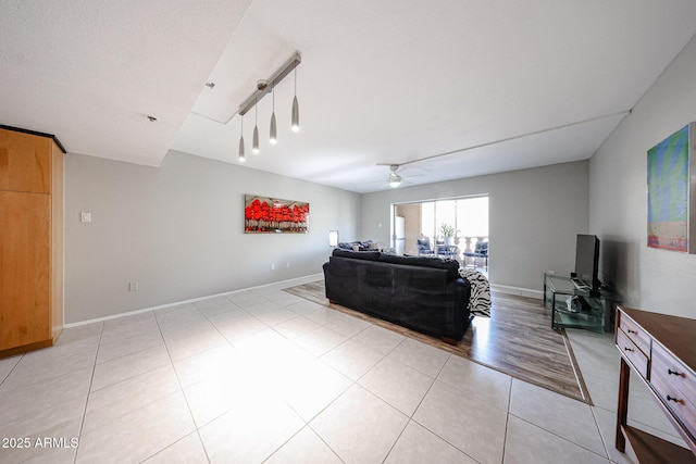 living area featuring baseboards, light tile patterned flooring, and a ceiling fan