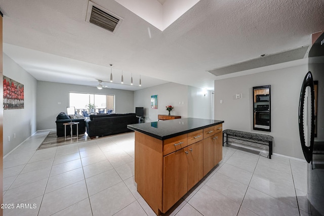 kitchen with visible vents, black appliances, dark countertops, a kitchen island, and light tile patterned floors