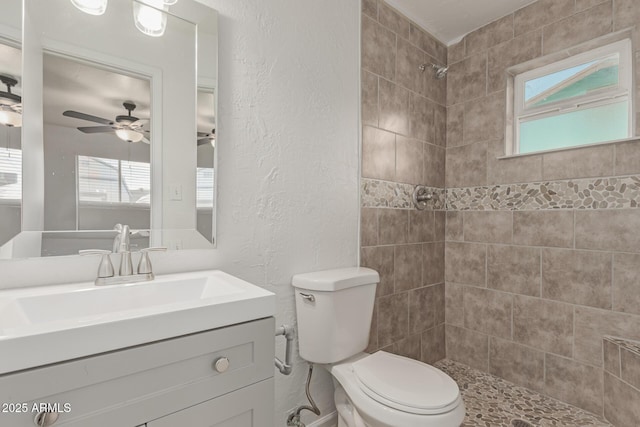 bathroom with vanity, tiled shower, ceiling fan, and toilet