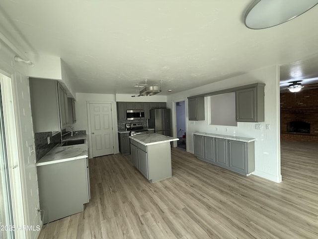 kitchen with sink, light hardwood / wood-style flooring, gray cabinets, a kitchen island, and stainless steel appliances