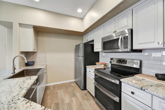 kitchen featuring light stone countertops, appliances with stainless steel finishes, tasteful backsplash, sink, and white cabinetry