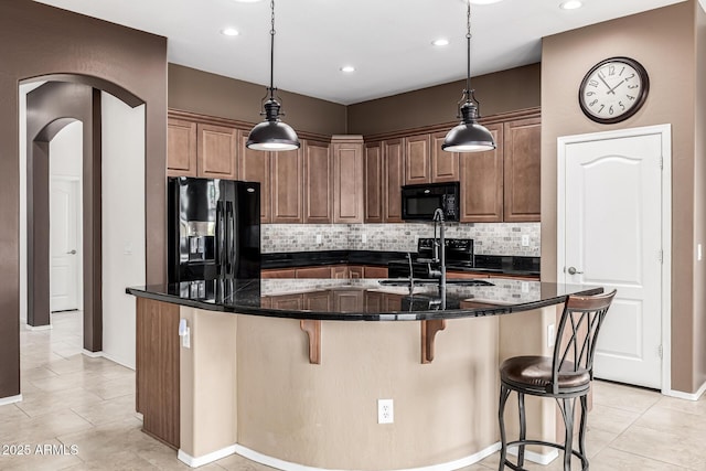 kitchen featuring a breakfast bar area, decorative backsplash, a sink, a large island, and black appliances