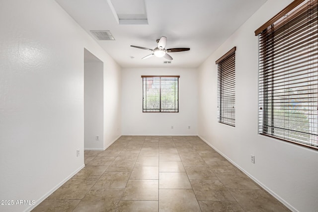 tiled spare room featuring baseboards, ceiling fan, and visible vents