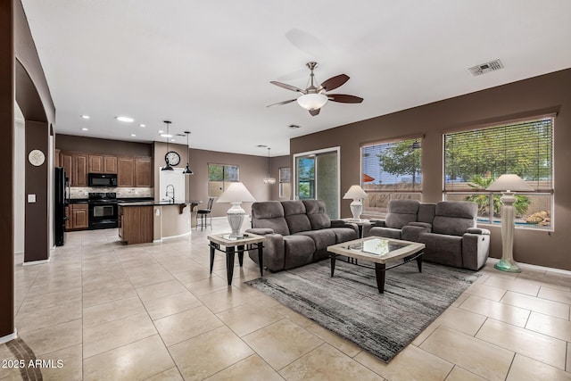 living area with light tile patterned floors, a wealth of natural light, visible vents, and a ceiling fan