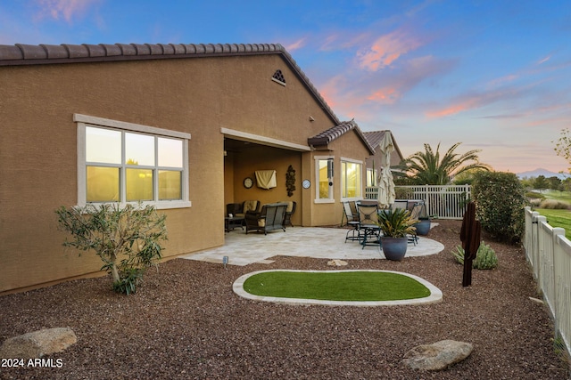 back of house at dusk featuring a fenced backyard, stucco siding, and a patio area