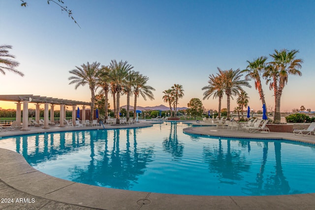 pool at dusk with a patio area and a pergola