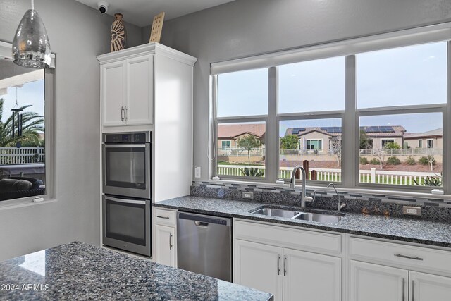 kitchen with appliances with stainless steel finishes, white cabinets, sink, and dark stone counters