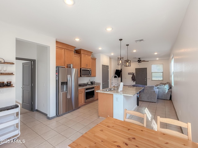 kitchen featuring ceiling fan, stainless steel appliances, an island with sink, decorative light fixtures, and light tile patterned flooring