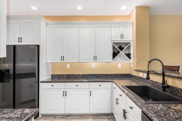 kitchen with dark stone countertops, white cabinetry, stainless steel refrigerator with ice dispenser, and a sink