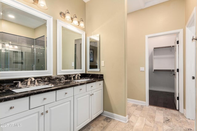 full bathroom with a sink, baseboards, double vanity, and a shower stall