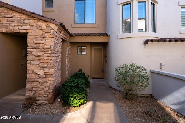 view of exterior entry with a tiled roof, stone siding, and stucco siding