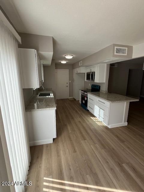 kitchen with hardwood / wood-style floors, black range oven, white cabinets, sink, and light stone counters