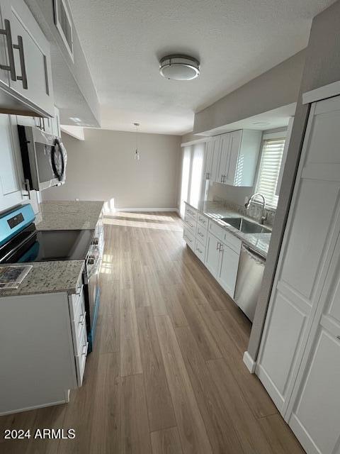 kitchen with light stone counters, stainless steel appliances, sink, hardwood / wood-style flooring, and white cabinets