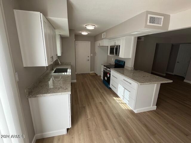 kitchen with black stove, white cabinetry, kitchen peninsula, and light hardwood / wood-style flooring