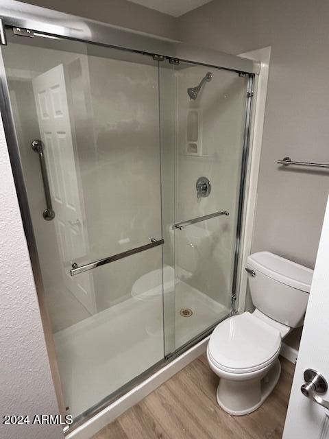 bathroom featuring wood-type flooring, toilet, and a shower with shower door