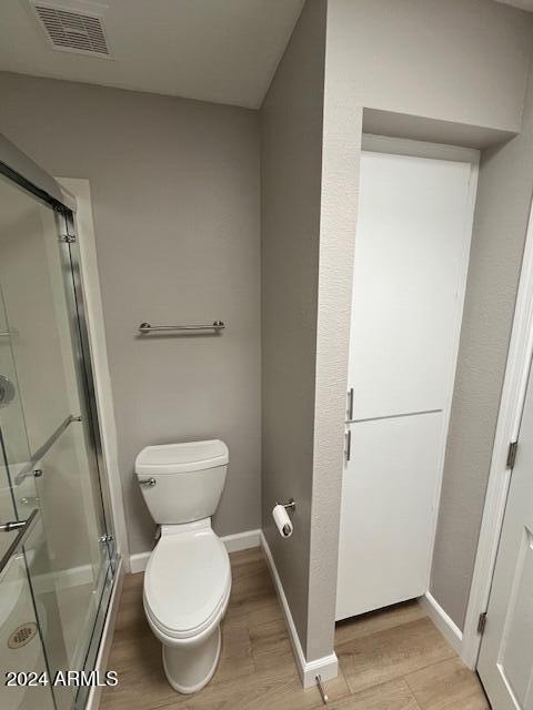 bathroom with hardwood / wood-style floors, toilet, and a shower with door