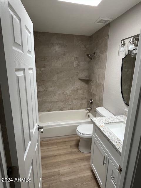 full bathroom with hardwood / wood-style floors, vanity, tiled shower / bath combo, and toilet