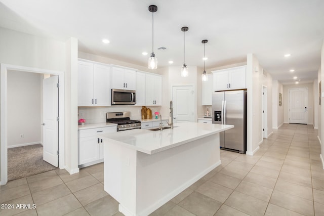 kitchen with stainless steel appliances, white cabinets, sink, pendant lighting, and a center island with sink