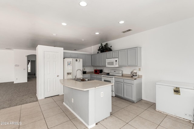 kitchen featuring gray cabinetry, white appliances, a kitchen island with sink, light carpet, and sink