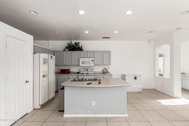 kitchen featuring white appliances, sink, an island with sink, gray cabinets, and light tile patterned flooring