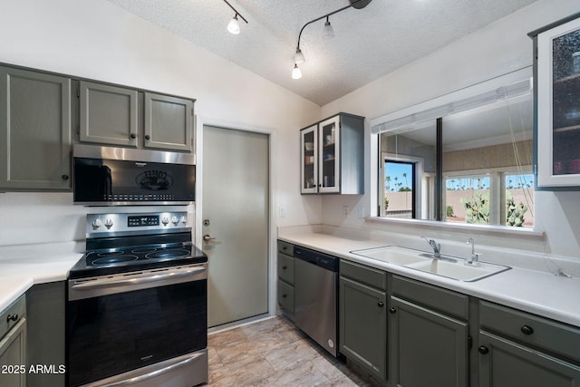 kitchen featuring gray cabinetry, a textured ceiling, stainless steel appliances, vaulted ceiling, and sink