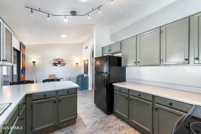 kitchen featuring a textured ceiling, black fridge, range, and kitchen peninsula