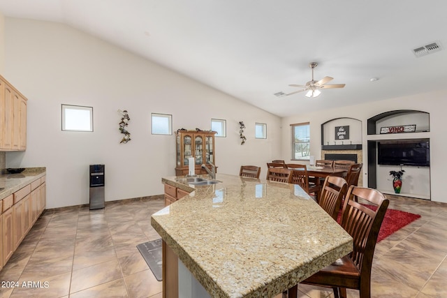 kitchen featuring ceiling fan, lofted ceiling, a kitchen bar, light brown cabinetry, and a center island with sink