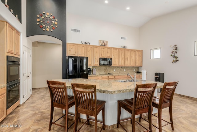 kitchen with light brown cabinets, high vaulted ceiling, black appliances, sink, and an island with sink