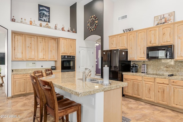 kitchen with a high ceiling, a kitchen breakfast bar, light brown cabinetry, and black appliances