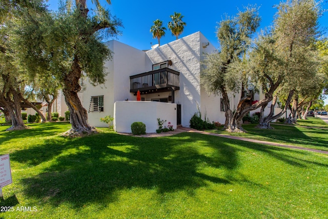 back of property with a lawn, a balcony, and stucco siding