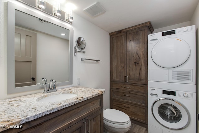 bathroom featuring estacked washer and dryer, vanity, toilet, and wood finished floors