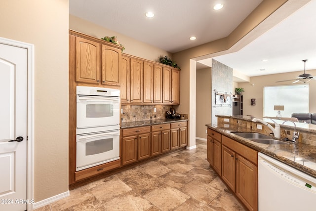 kitchen featuring tasteful backsplash, white appliances, ceiling fan, dark stone counters, and sink