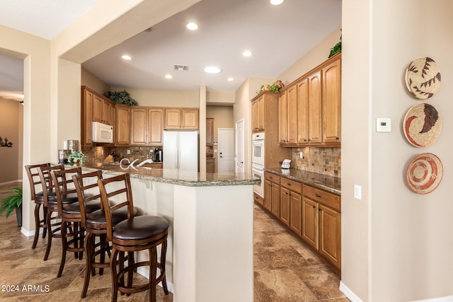 kitchen with kitchen peninsula, white appliances, stone countertops, a kitchen bar, and decorative backsplash