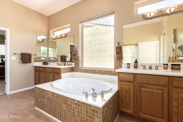 bathroom with a healthy amount of sunlight, tile patterned floors, tiled bath, and vanity