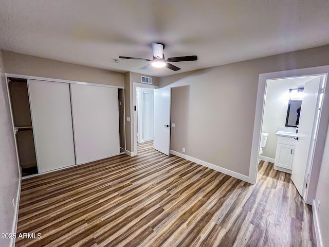 unfurnished bedroom featuring hardwood / wood-style floors, ensuite bathroom, a closet, and ceiling fan