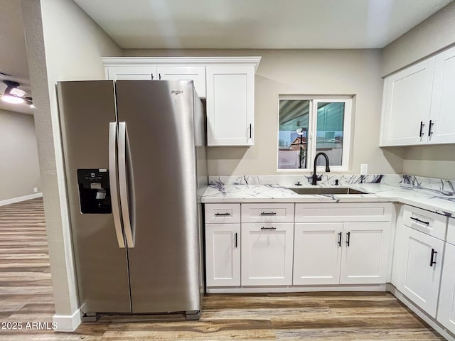 kitchen with white cabinets, stainless steel fridge, light stone counters, and sink