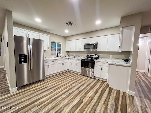 kitchen with light stone countertops, appliances with stainless steel finishes, sink, white cabinets, and light hardwood / wood-style floors